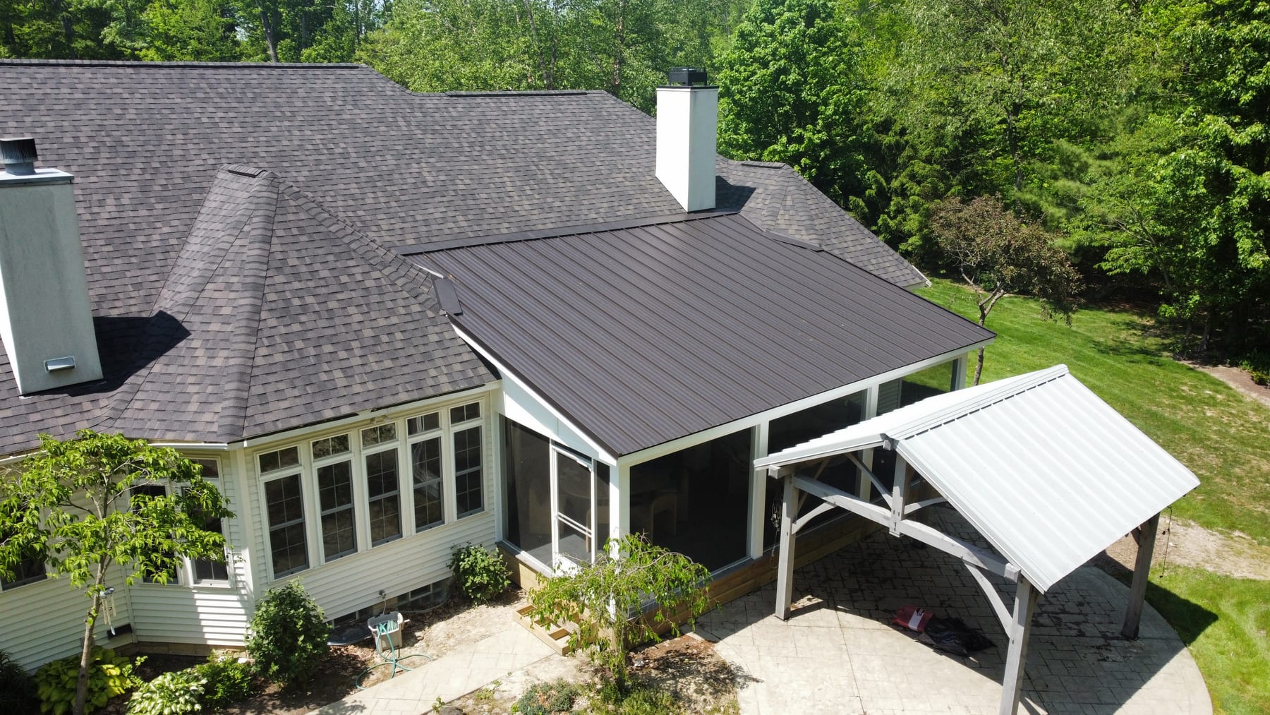 Aerial view of a finished home with a standing-seam metal roof, screened porch, and pergola