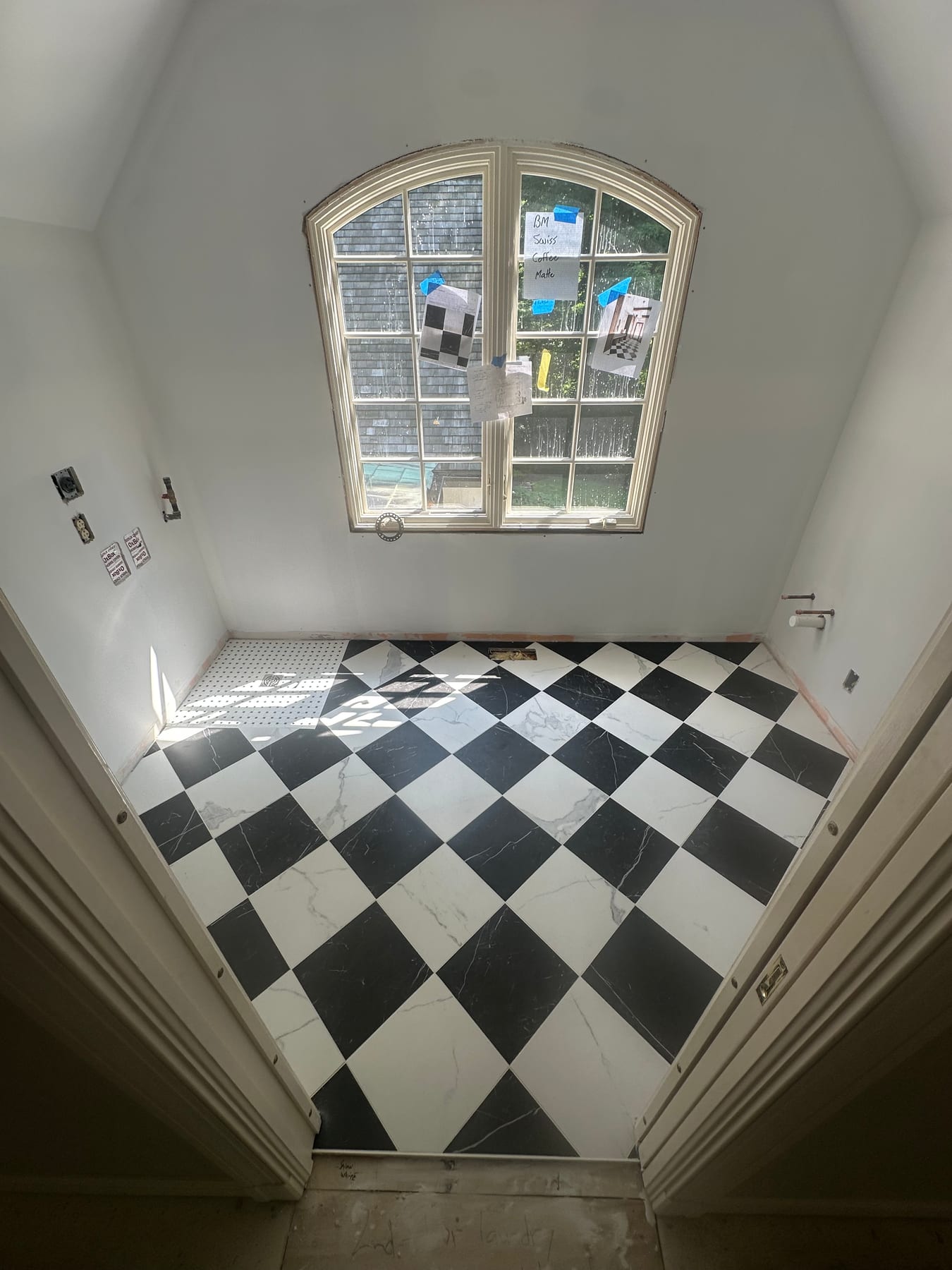 A black and white checkerboard tile floor mid-installation in a sunlit room