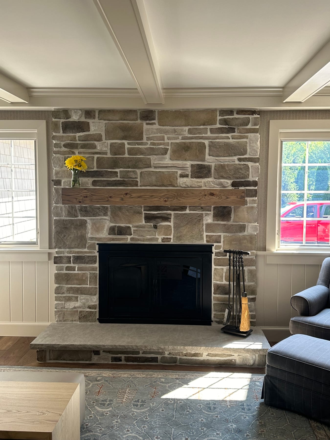 A stone fireplace with a reclaimed wood mantel between two windows
