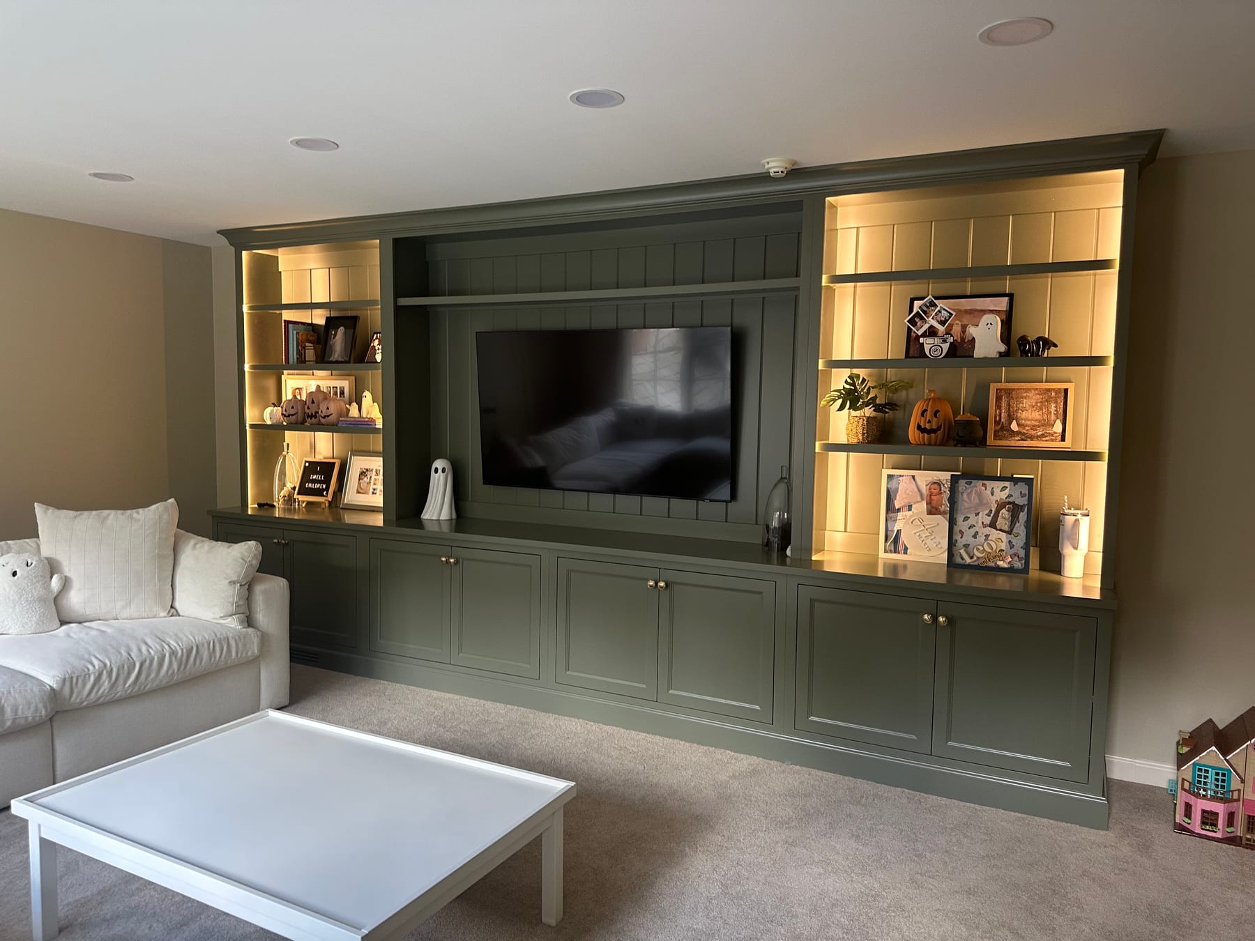 A green built-in media wall with lit display shelving and cabinetry around a TV