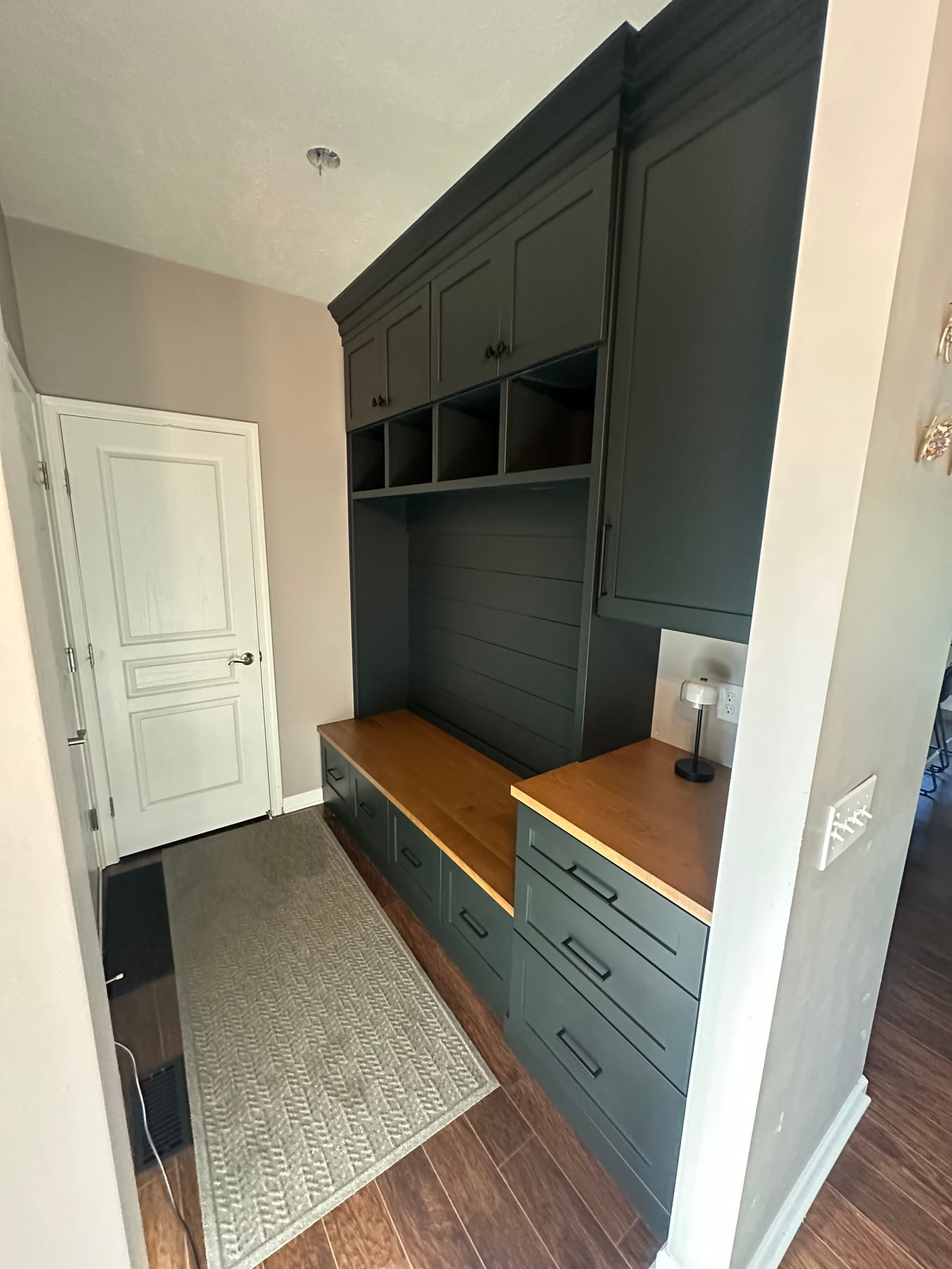 A mudroom bench and cubbies in deep green cabinetry with a wood seat
