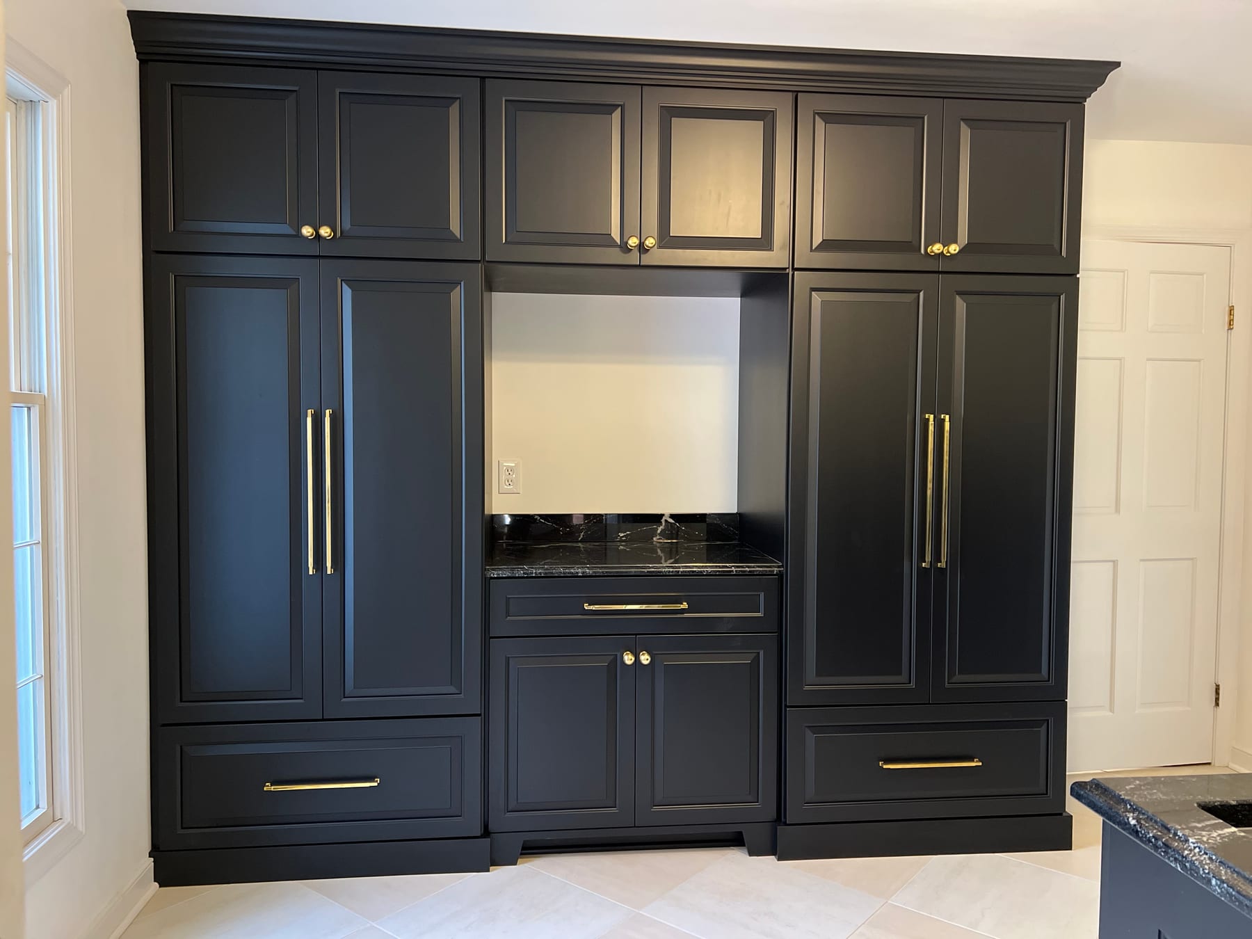 A wall of dark painted pantry cabinetry with brass hardware