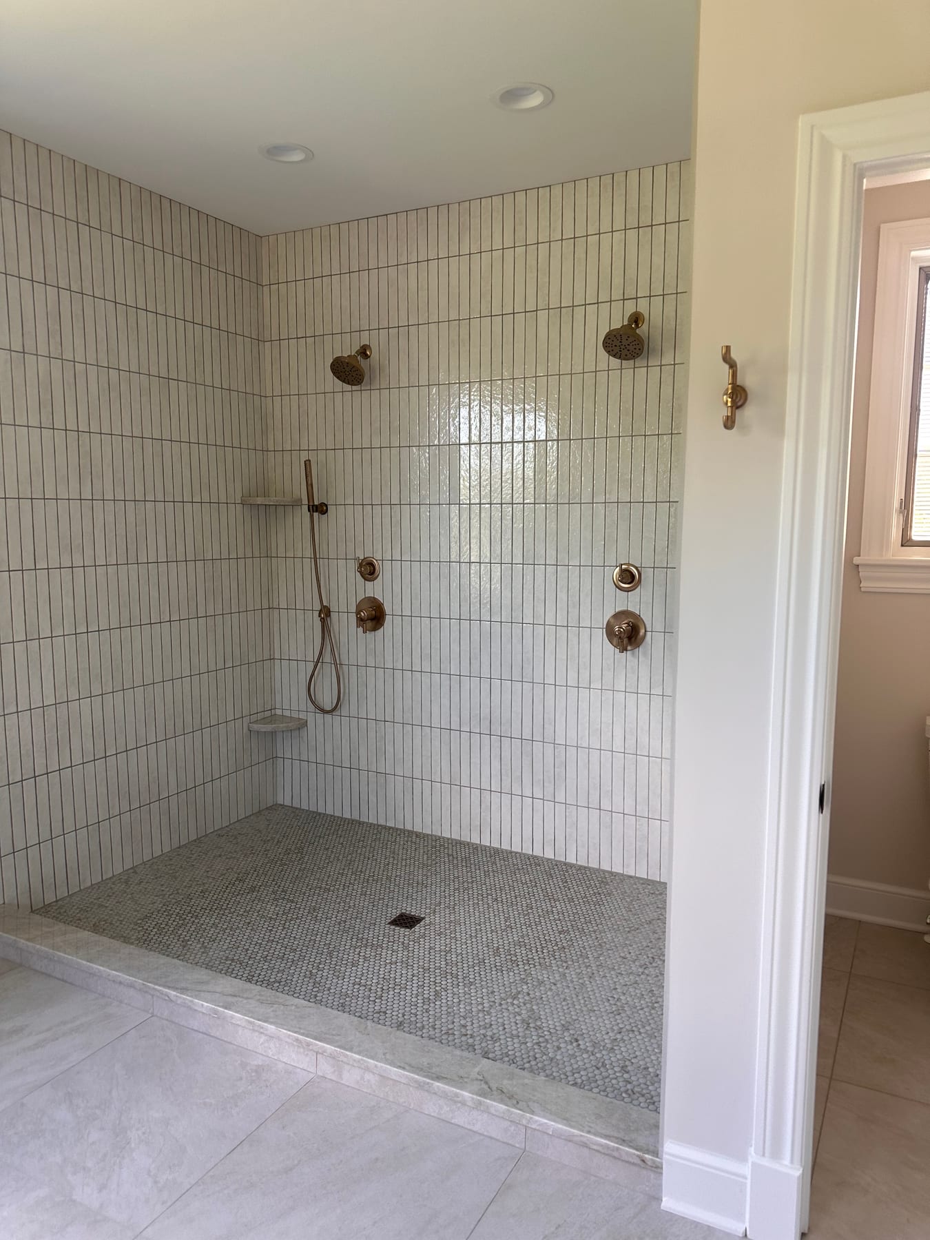 A walk-in shower in vertical white tile with brass fixtures and a mosaic floor