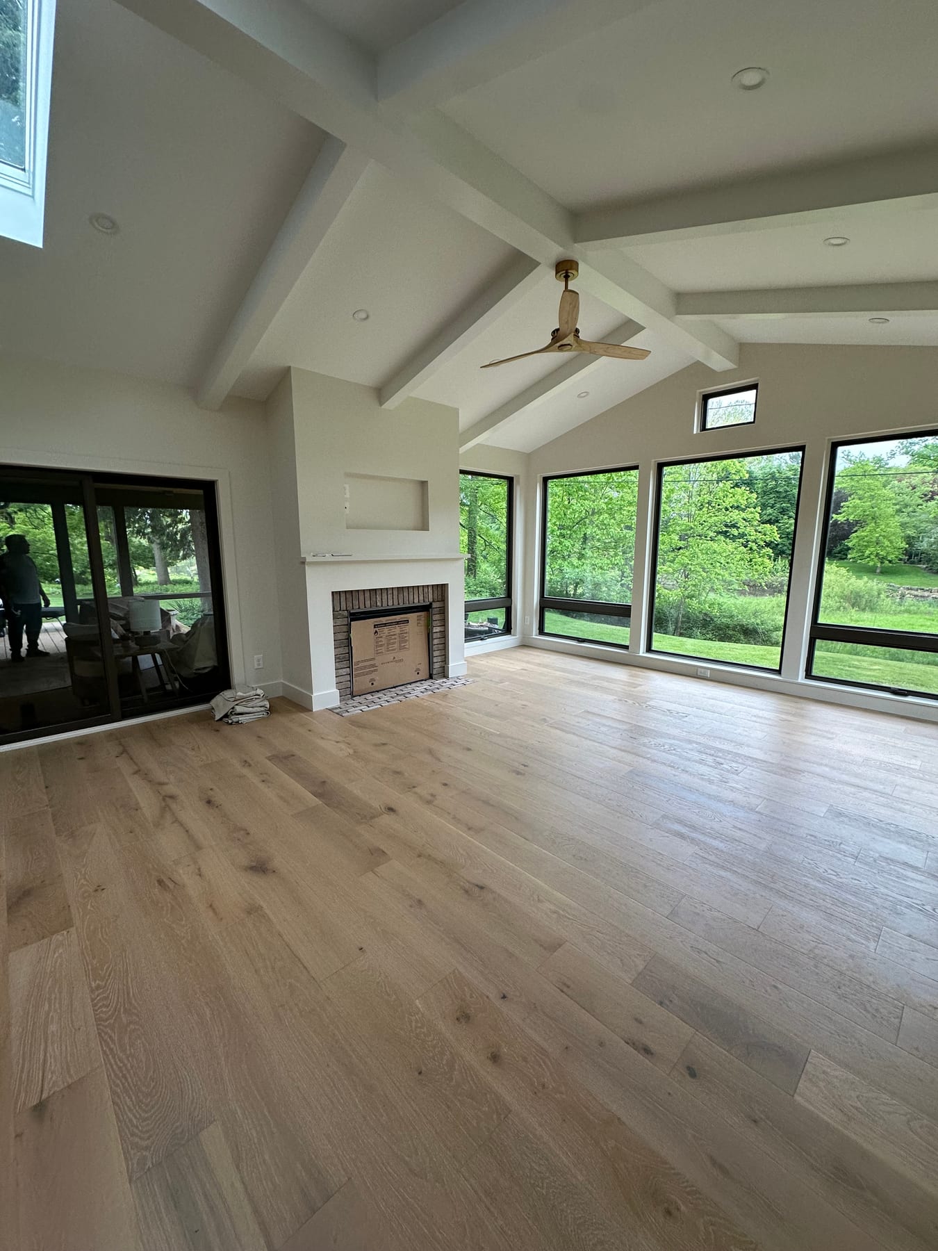 A vaulted sunroom with a fireplace, white oak floors, and walls of black-framed windows